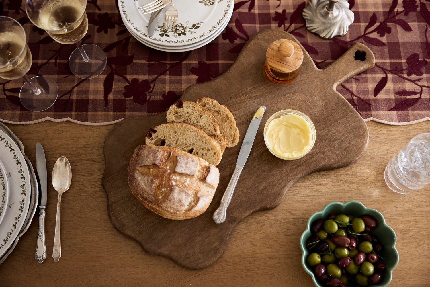 Shop Serving Boards + Platters. Image features wooden serving platter on table with bread loaf.
