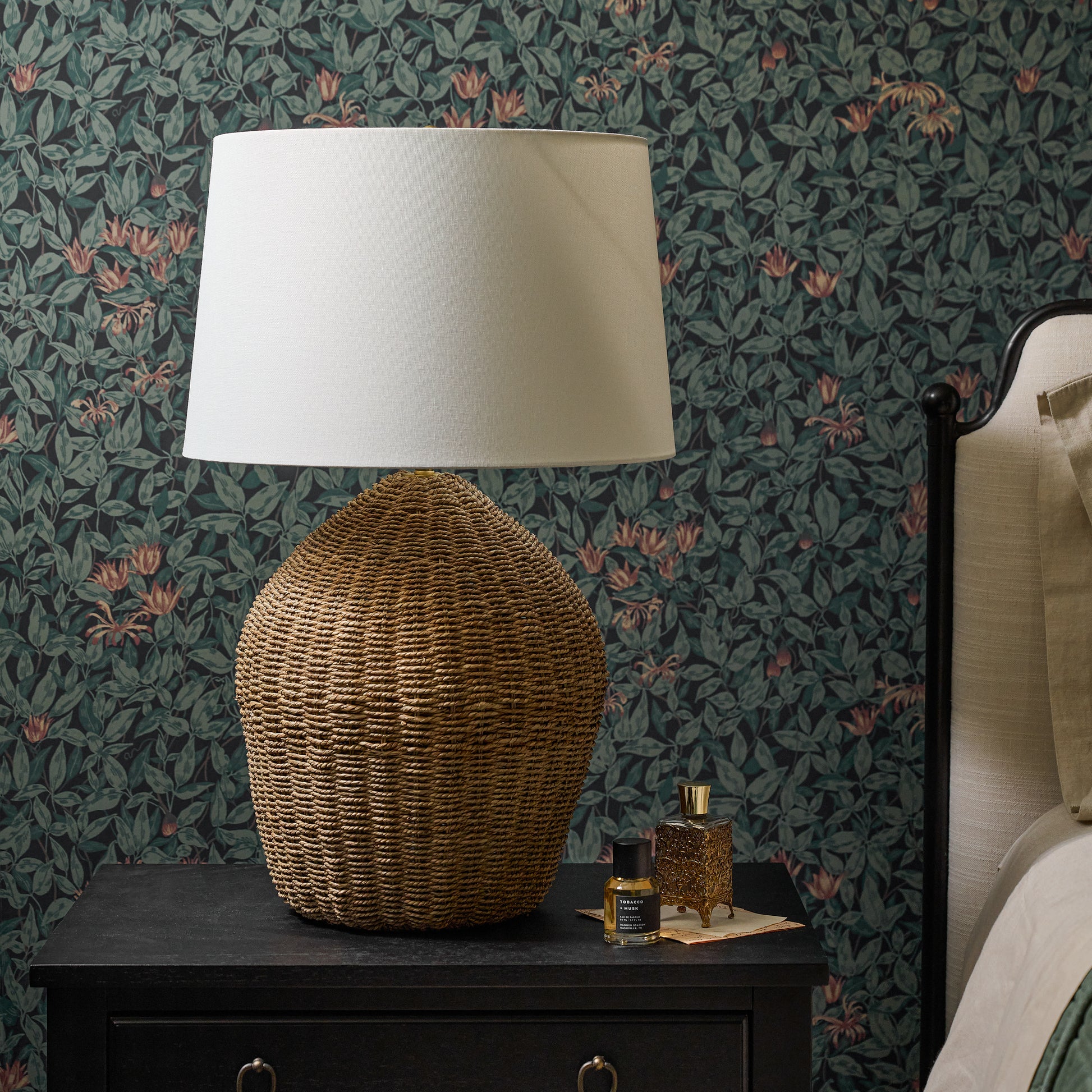 Tia Natural Rattan Table Lamp on a black nightstand against floral wallpaper