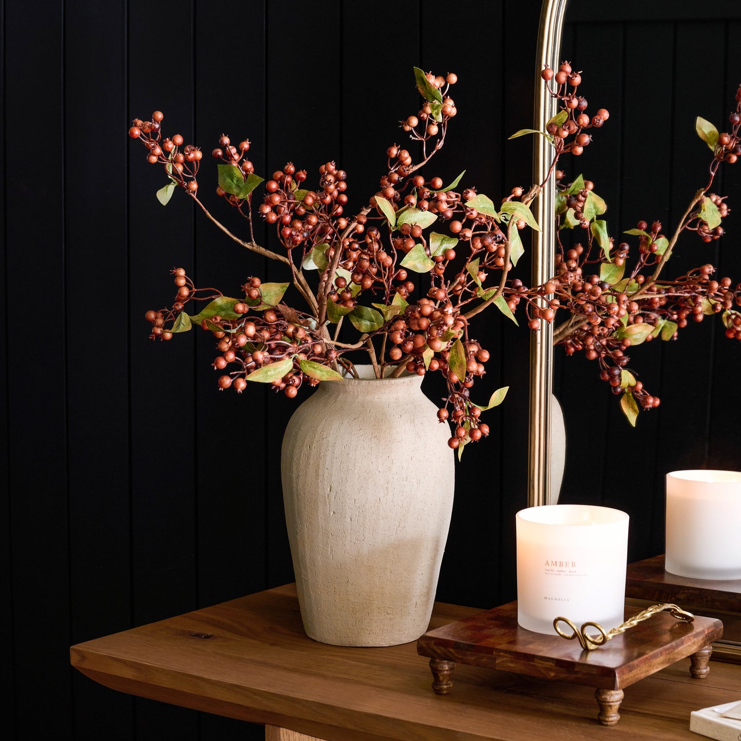 Brown Berry Spray with Green Leaves in a vase on a table next to a candle