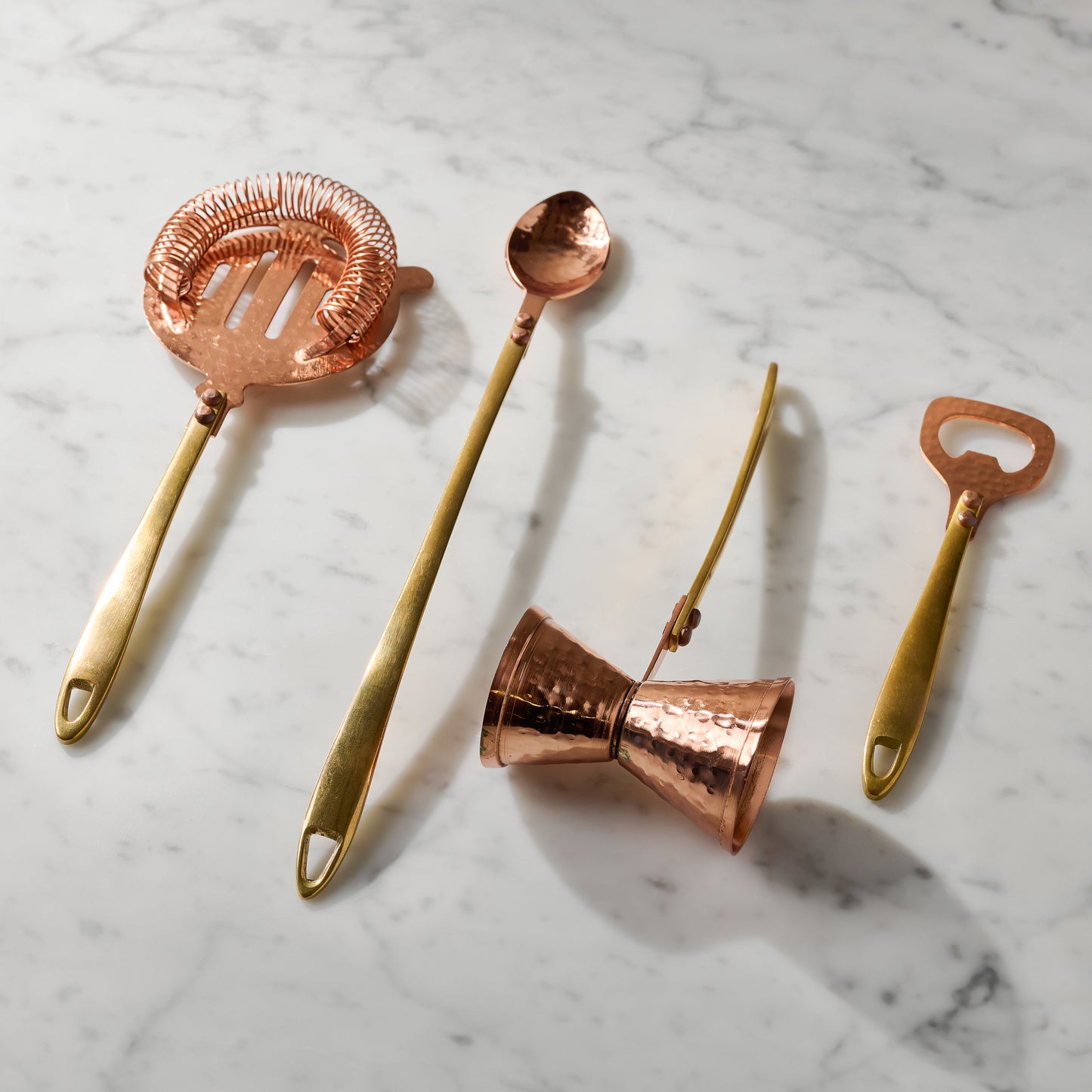 Hammered Copper and Gold Jigger shown with other bar tools on marble counter