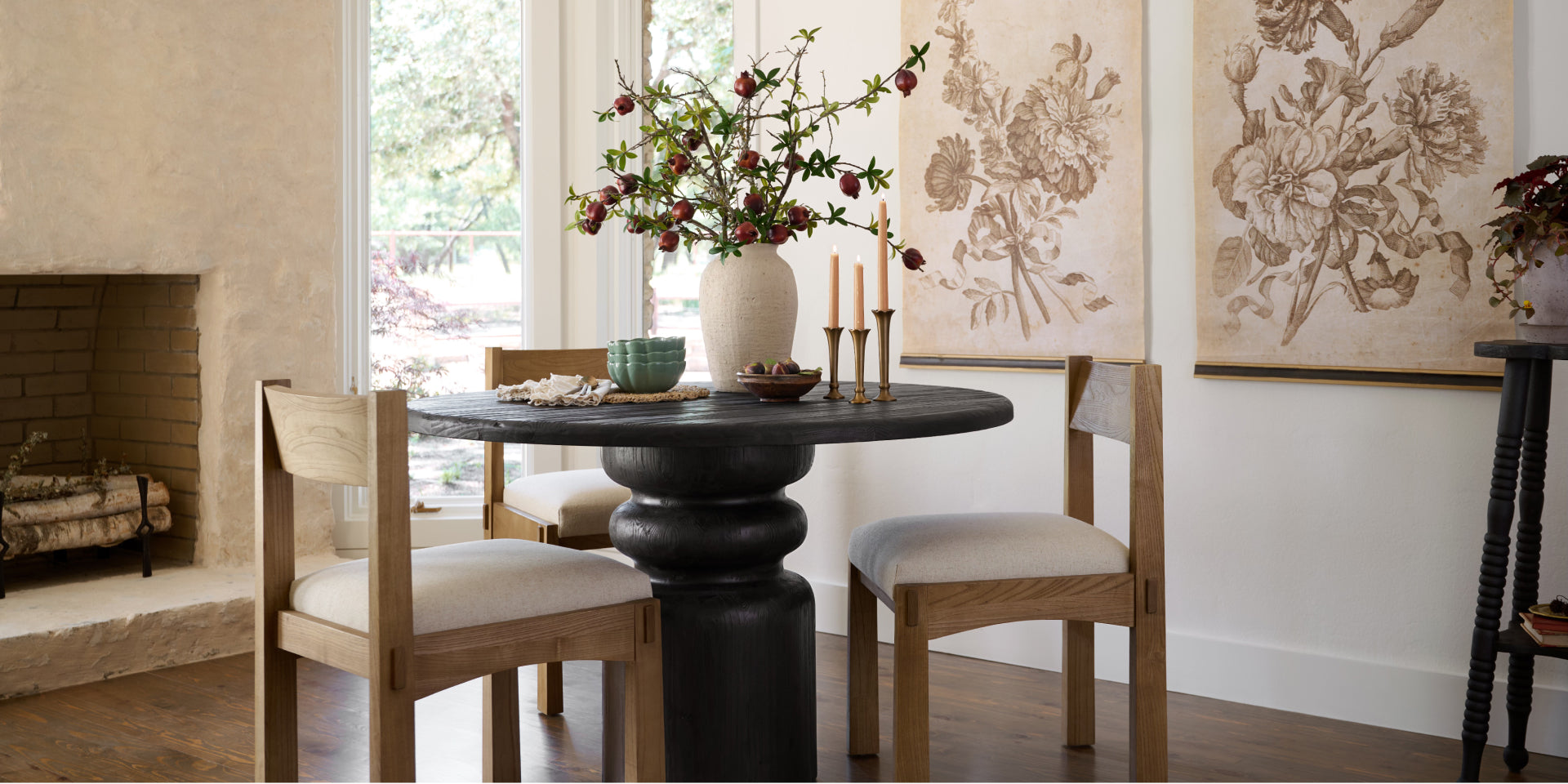 Dining room with a round black table and wooden chairs, featuring a vase of flowers and framed artwork. Shop New Arrivals.