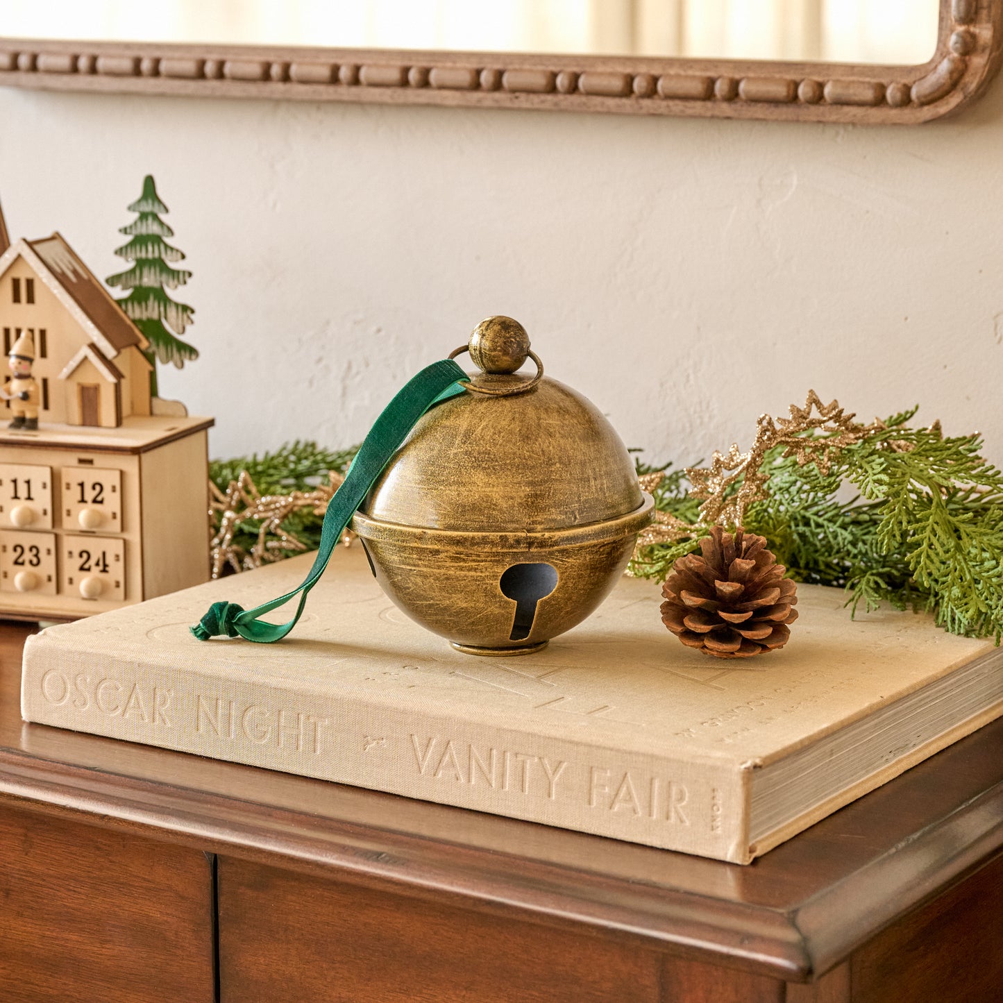 Antiqued Brass Jingle Bell Sit About swhown styled on book next to pinecone