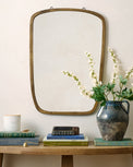 Jameson Aged Brass Framed Mirror on the wall above console tab with coffee tables, candle and floral vase