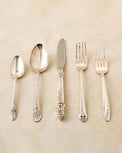 Set of silverware including spoons, a knife, and forks on a beige background
