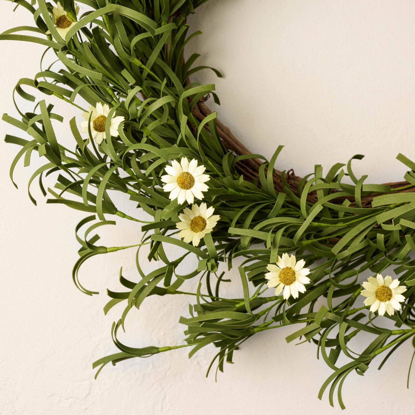 close up view of leafy green wreath with small faux daisies