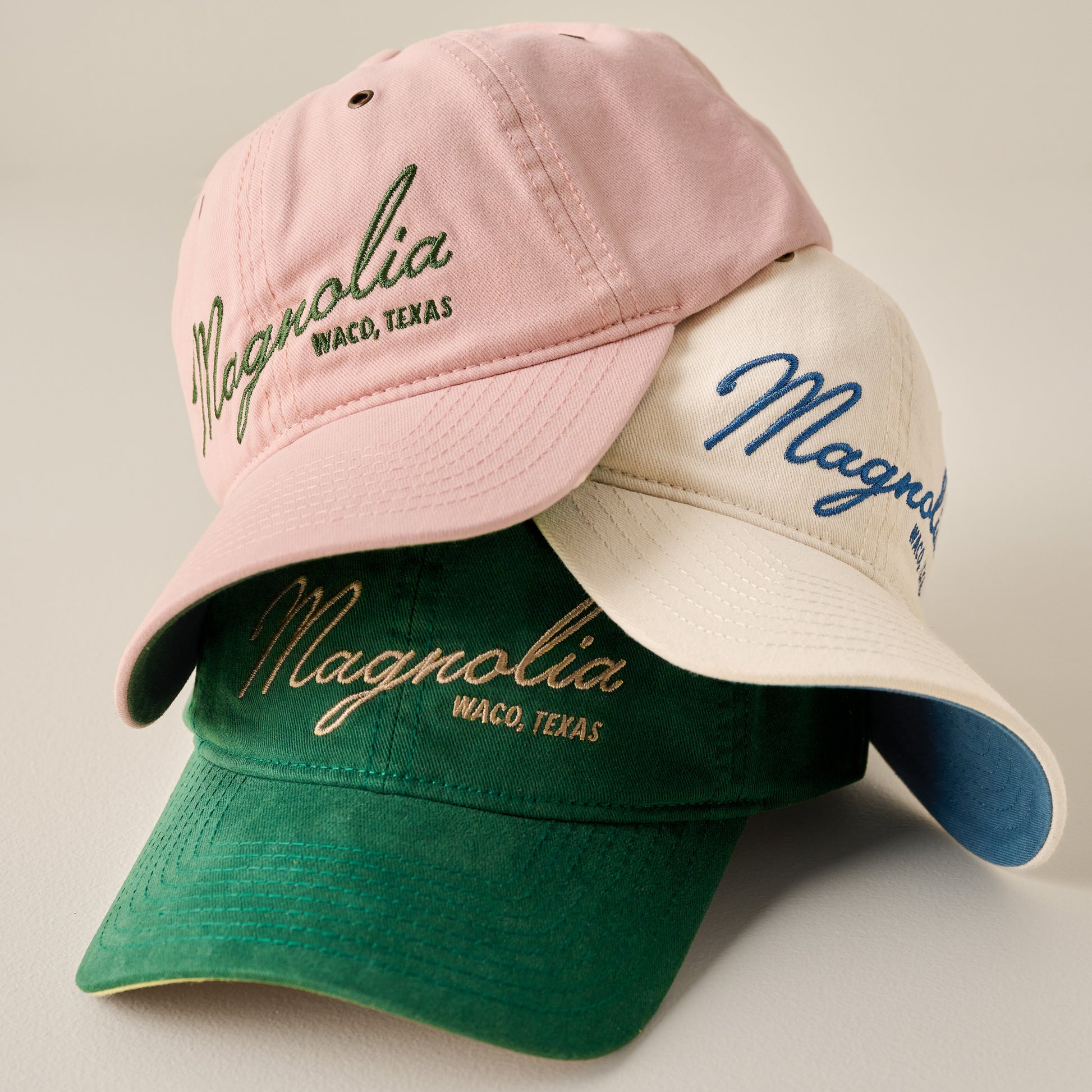 Magnolia Embroidered Script Cream Hat shown with green and pink hats