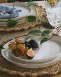 Table setting with white plates, grapes, and figs on a woven placemat.