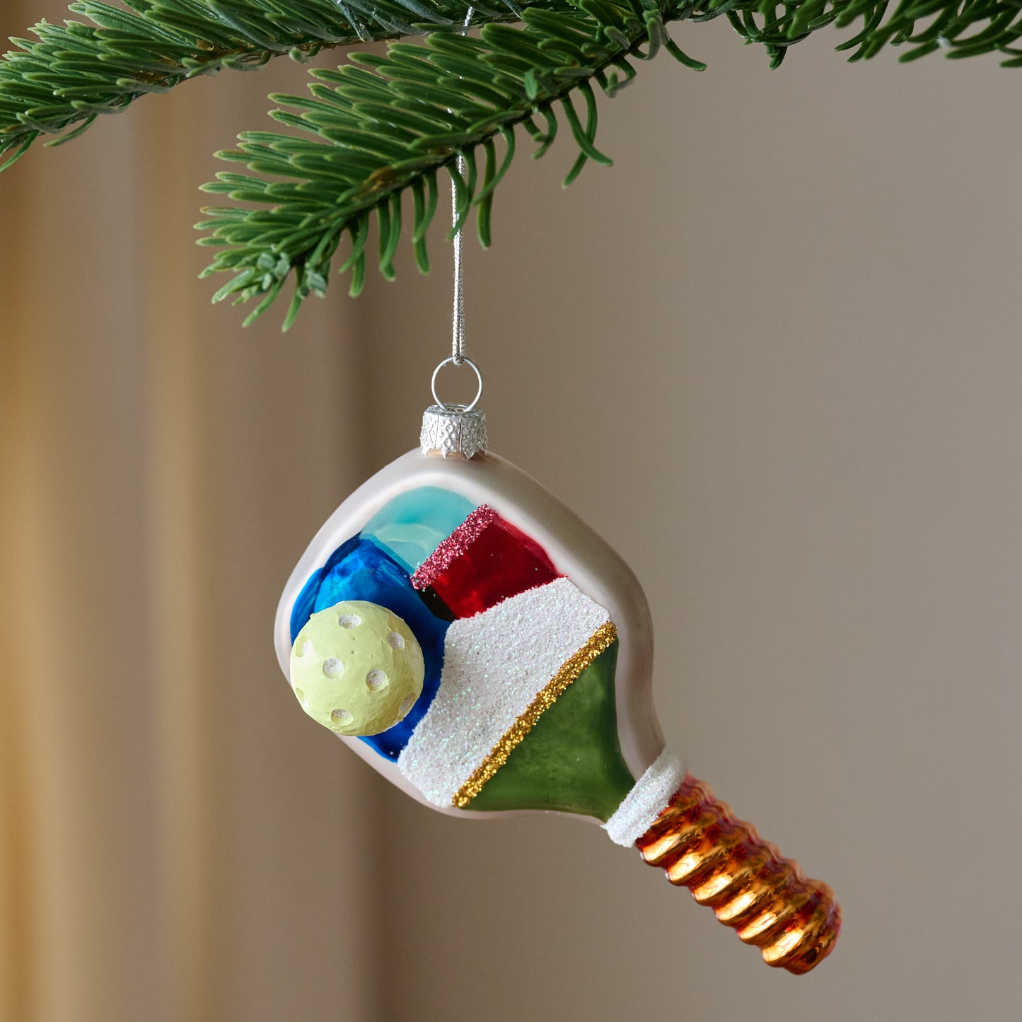 Painted Glass Pickleball Ornament shown hung on branch
