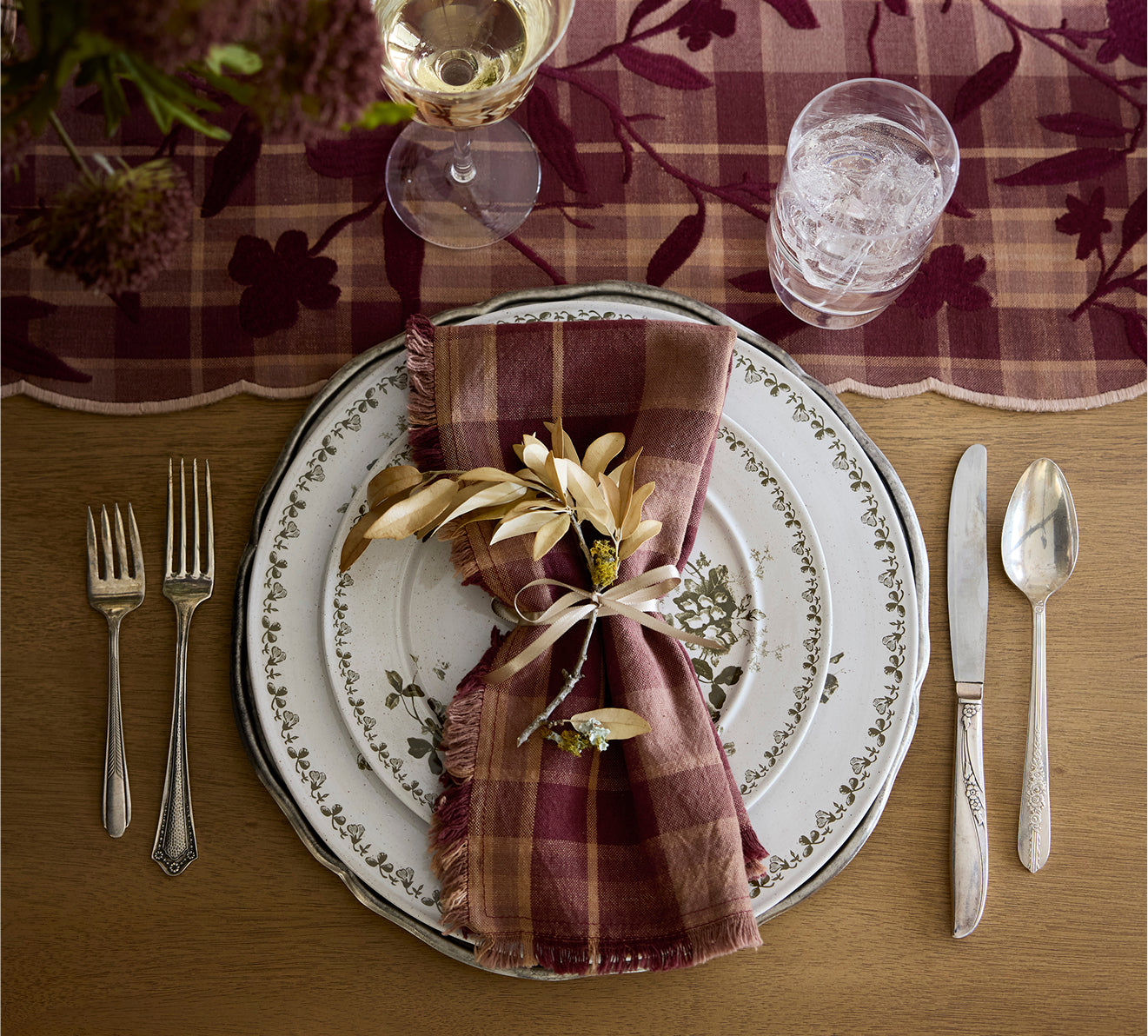 Dining table setting with decorative plates, cutlery, and a plaid napkin on a checkered tablecloth.