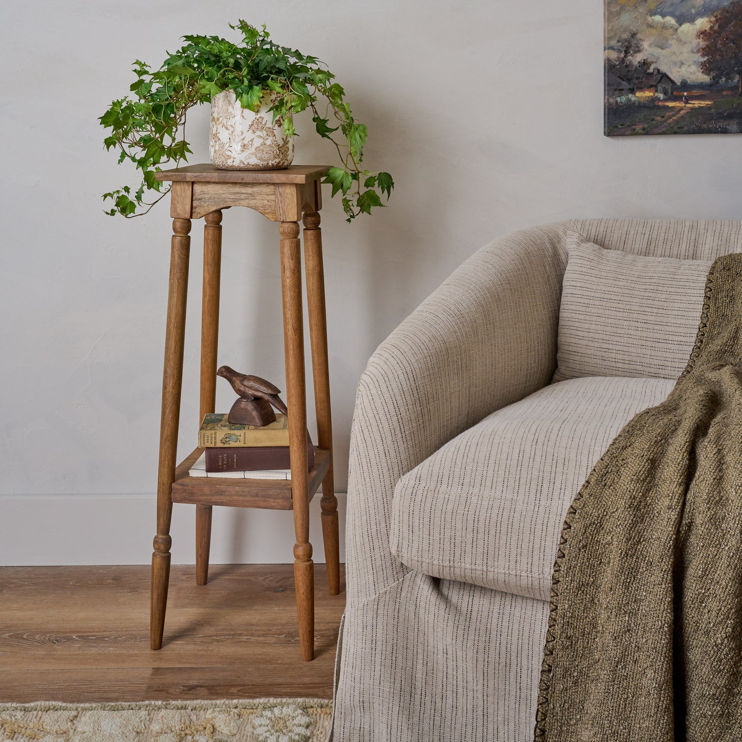 Cunningham Plant Stand shown next to upholstered chair with plant on top