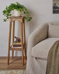 Cunningham Plant Stand shown next to upholstered chair with plant on top