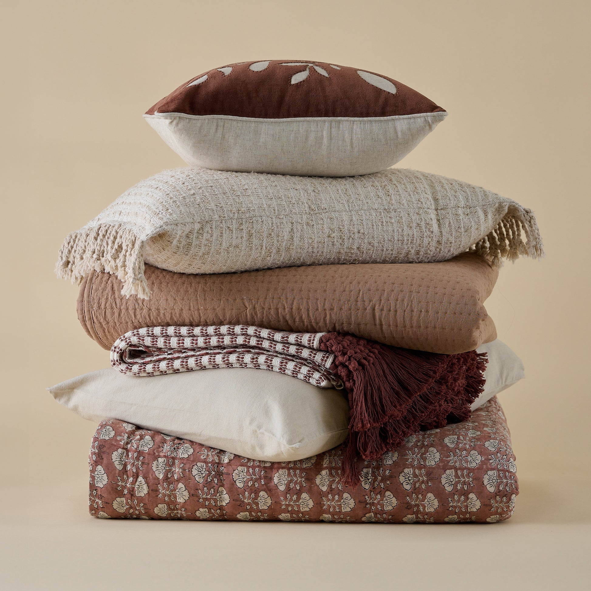 Essential Tassel Throw - Burgundy Striped shown folded in stack of pillows and bedding