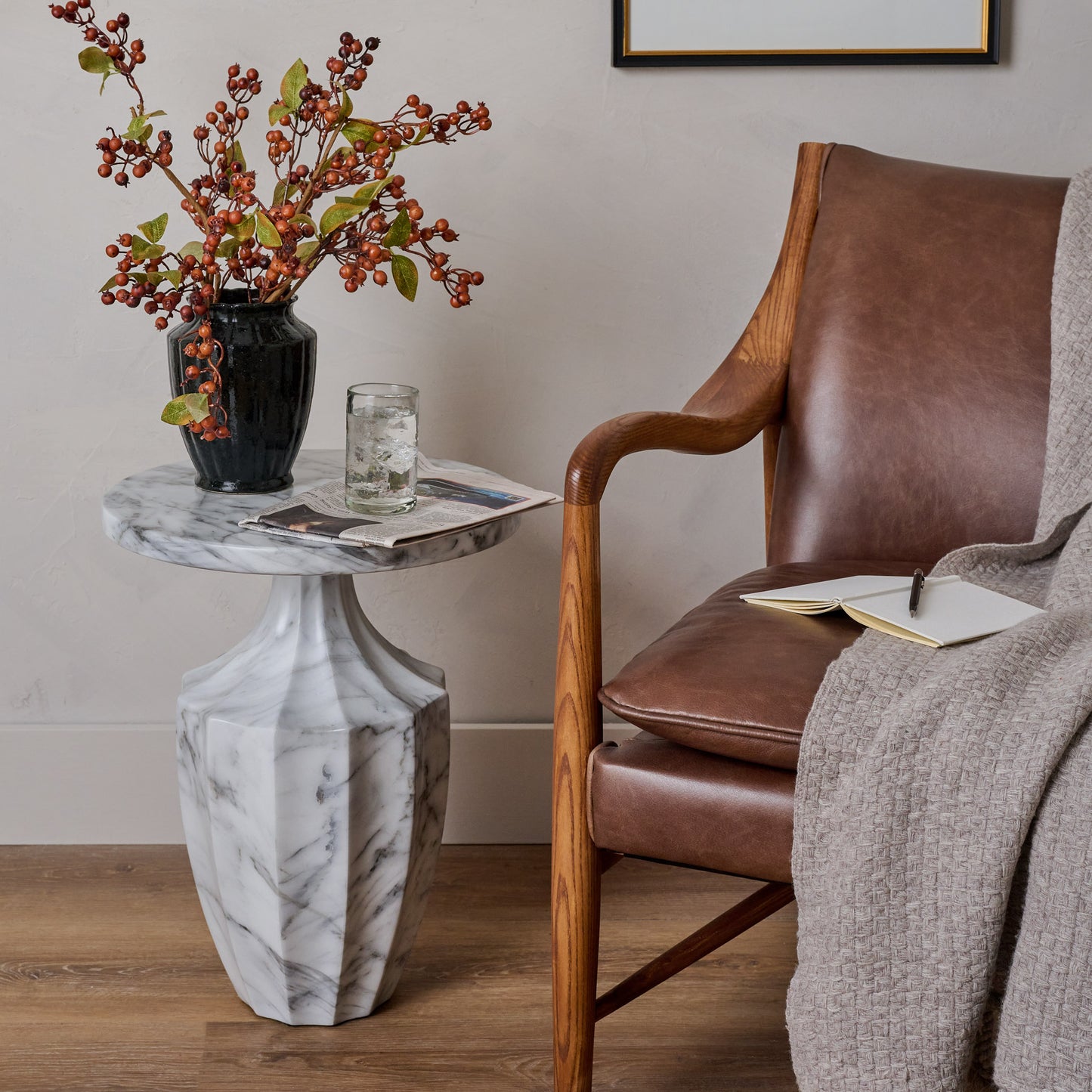Brown Berry Spray with Green Leaves shown in vase on side table next to chair