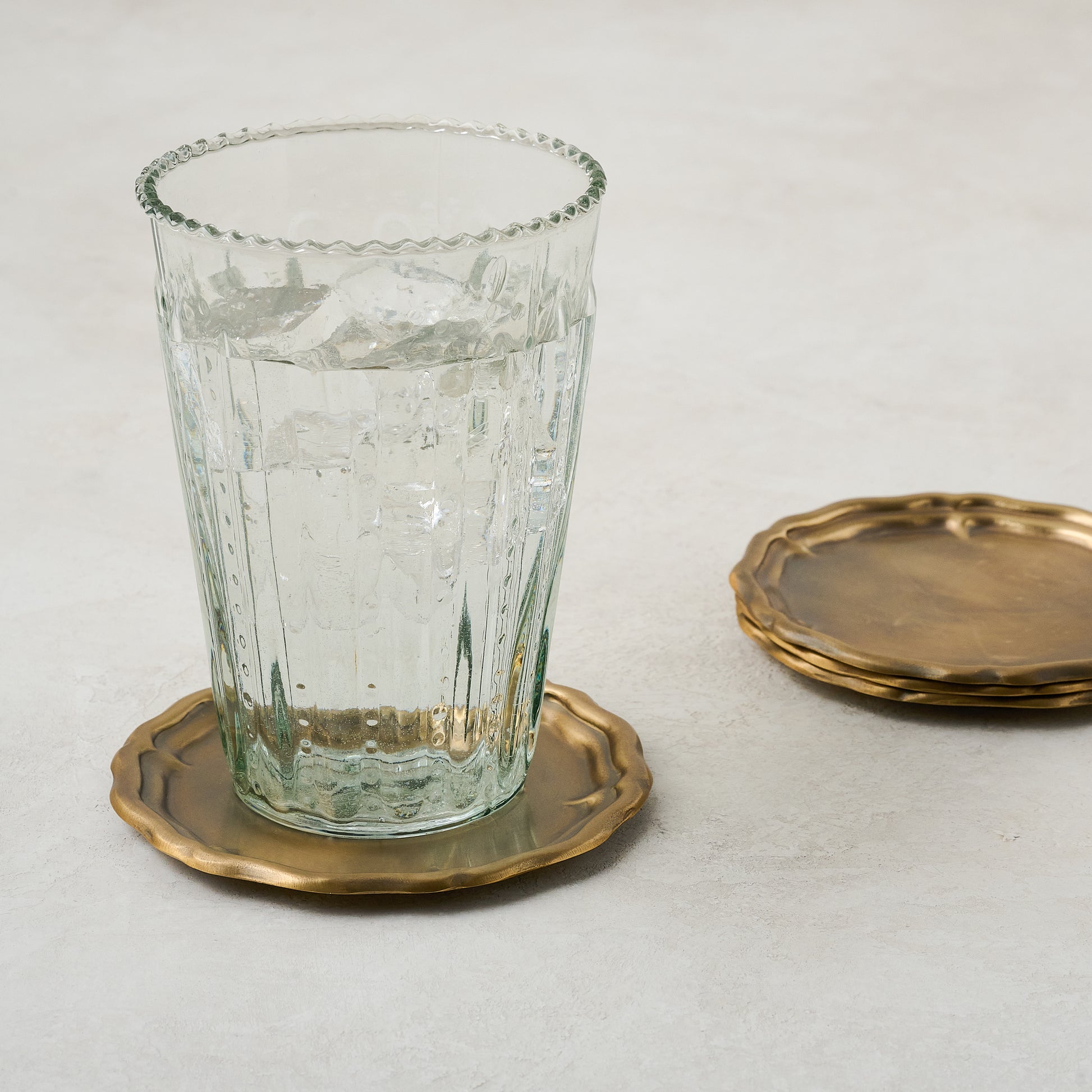 Vintage-Inspired Brass Coaster Set of Four shown with glass of water