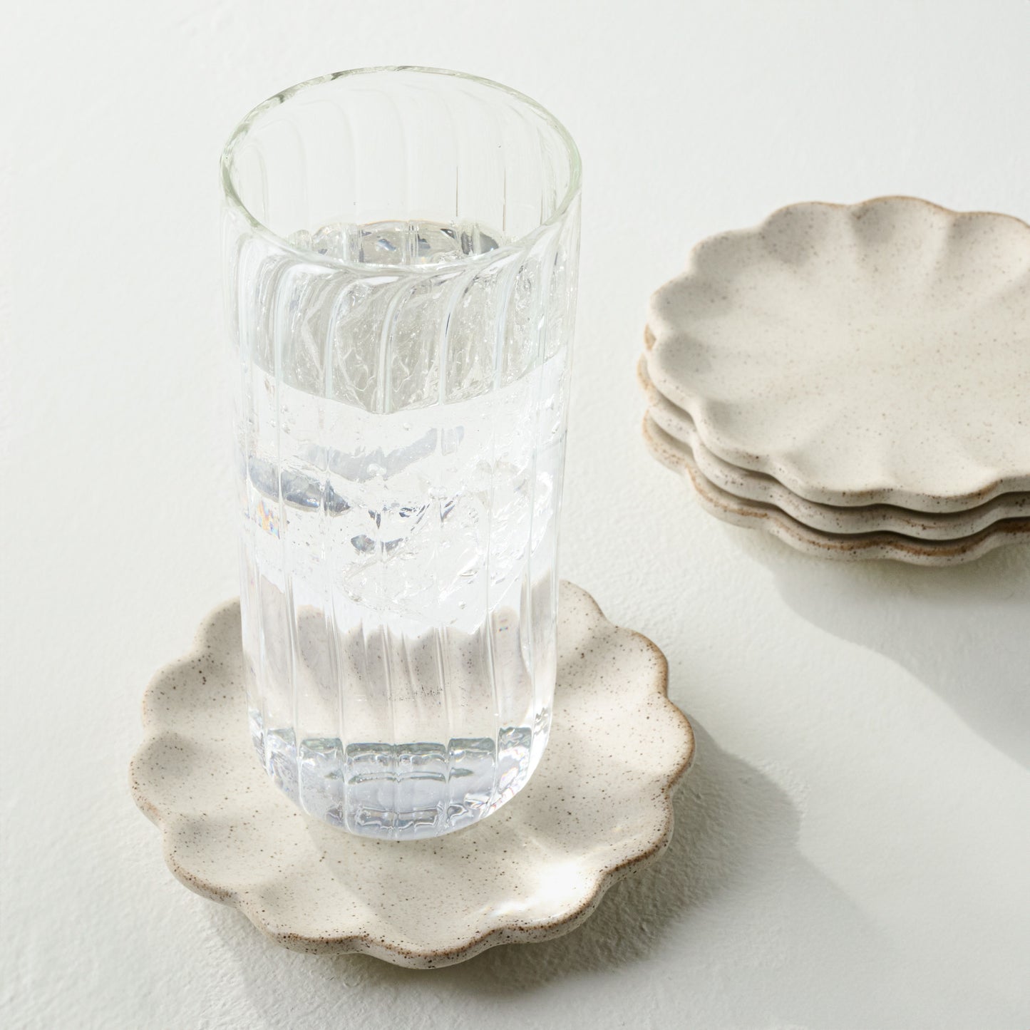 French White Scalloped Edge Stoneware Coaster Set shown with fluted glass