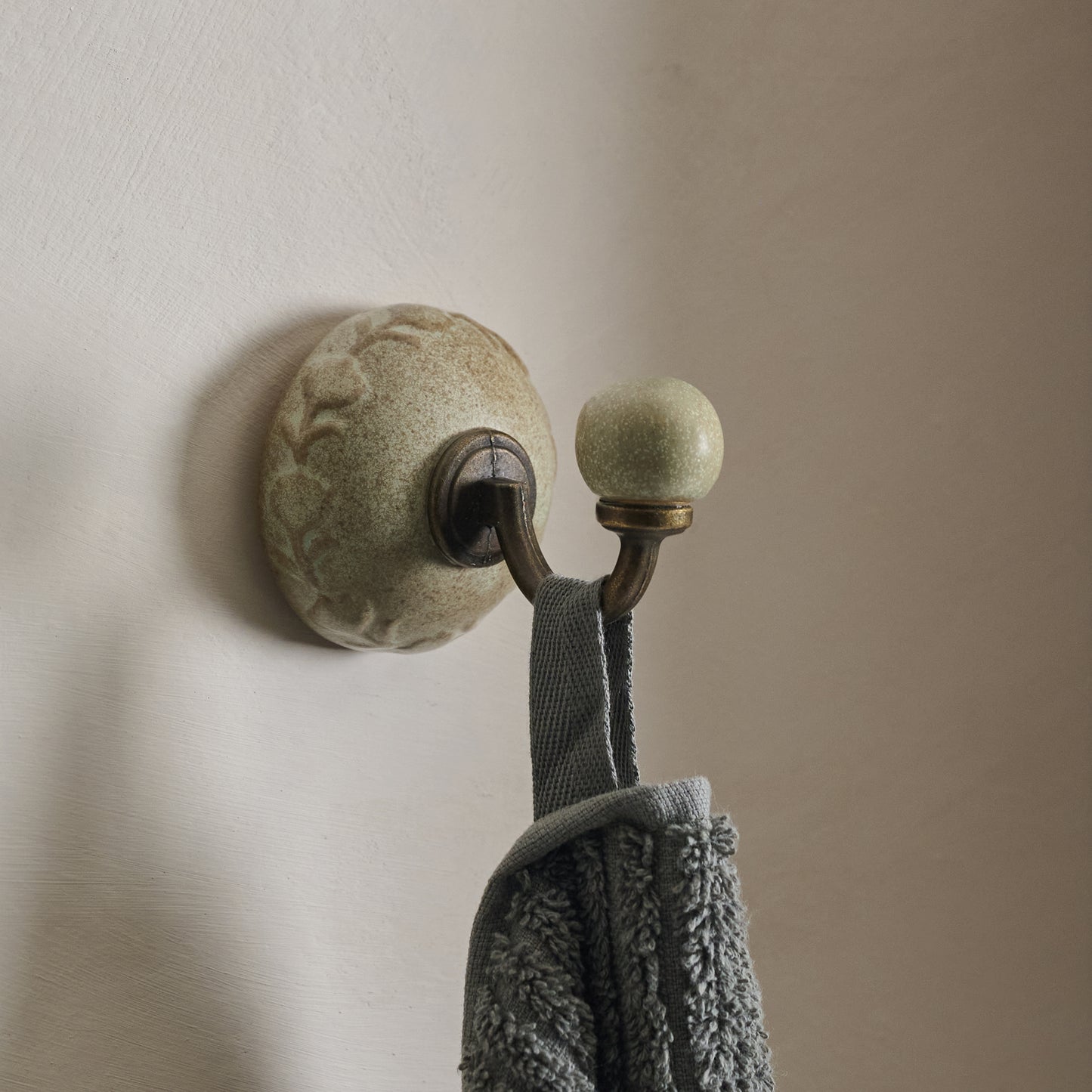 French Grey Emilie Floral Ceramic Wall Hook shown hung on wall with towel