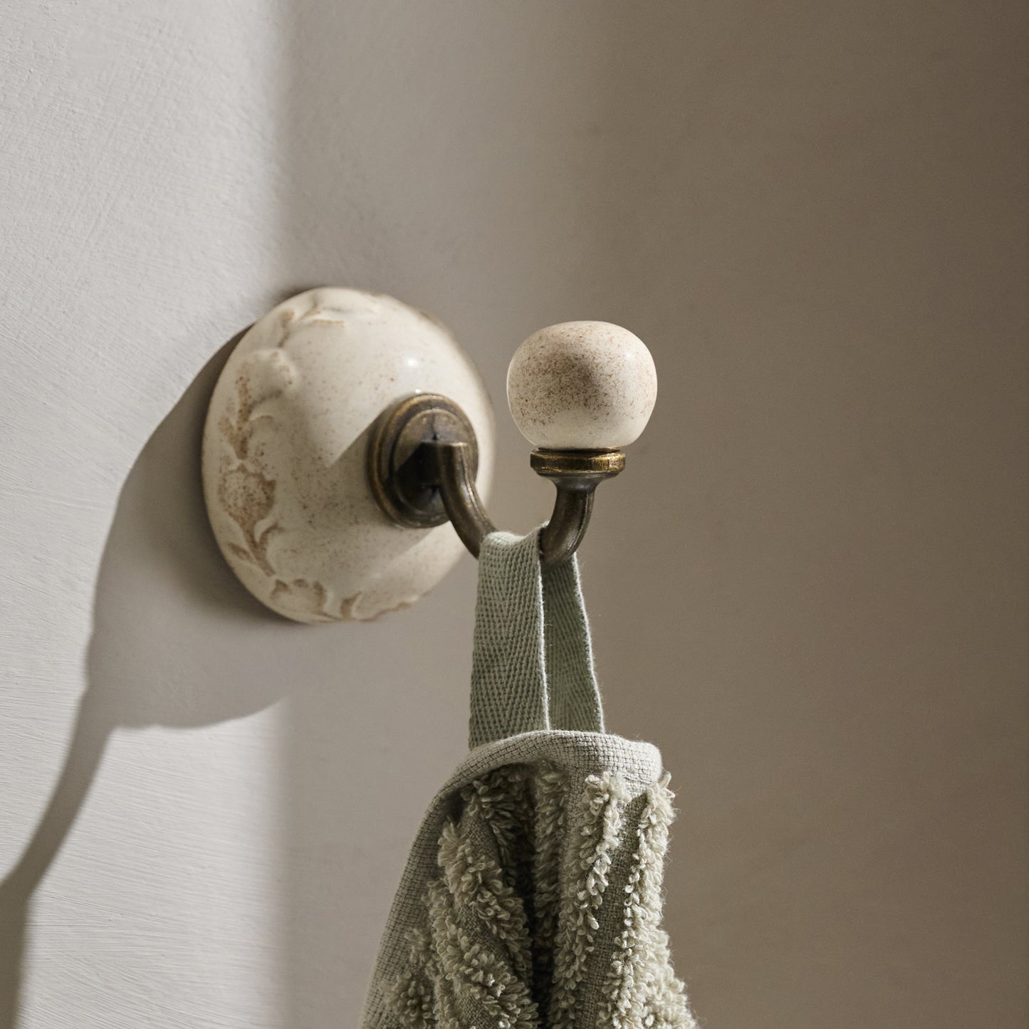French White Emilie Floral Ceramic Wall Hook shown hung on wall with towel