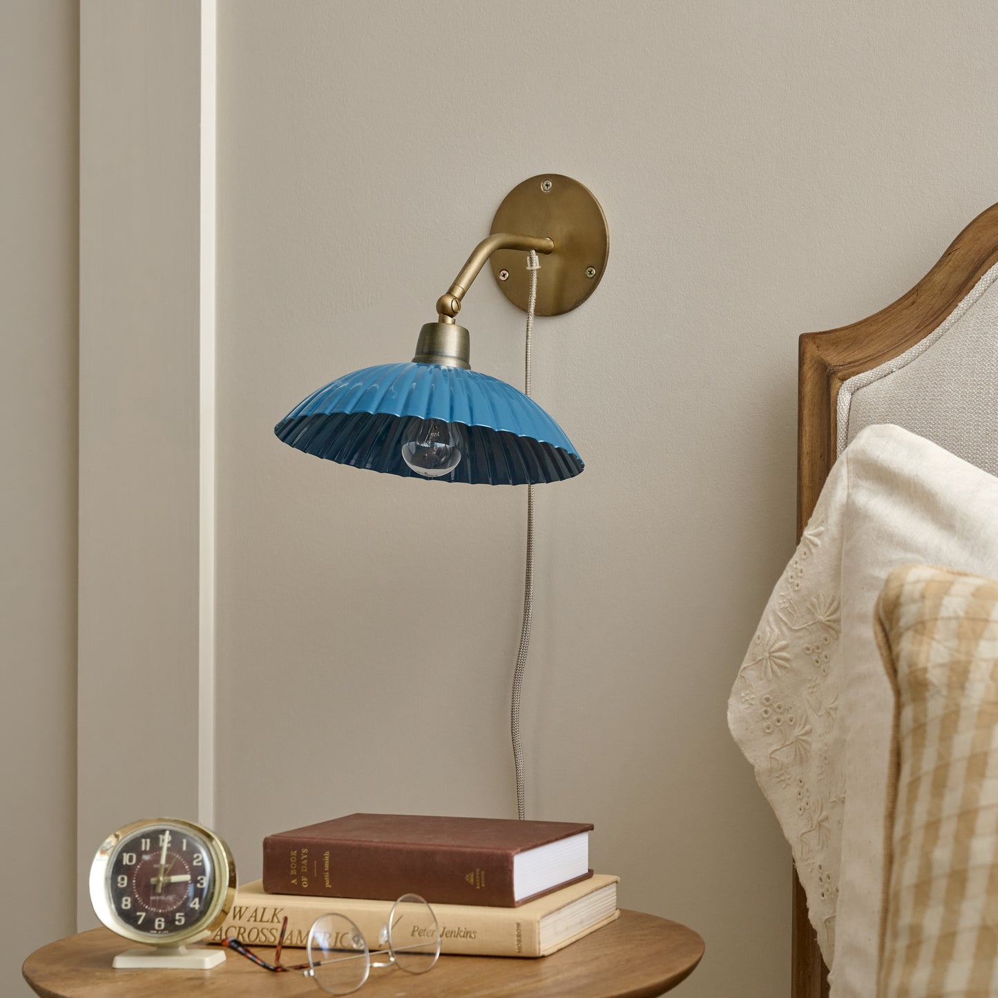Chester Enamel Plug-in Sconce - Blue with Brass shown on wall next to bed