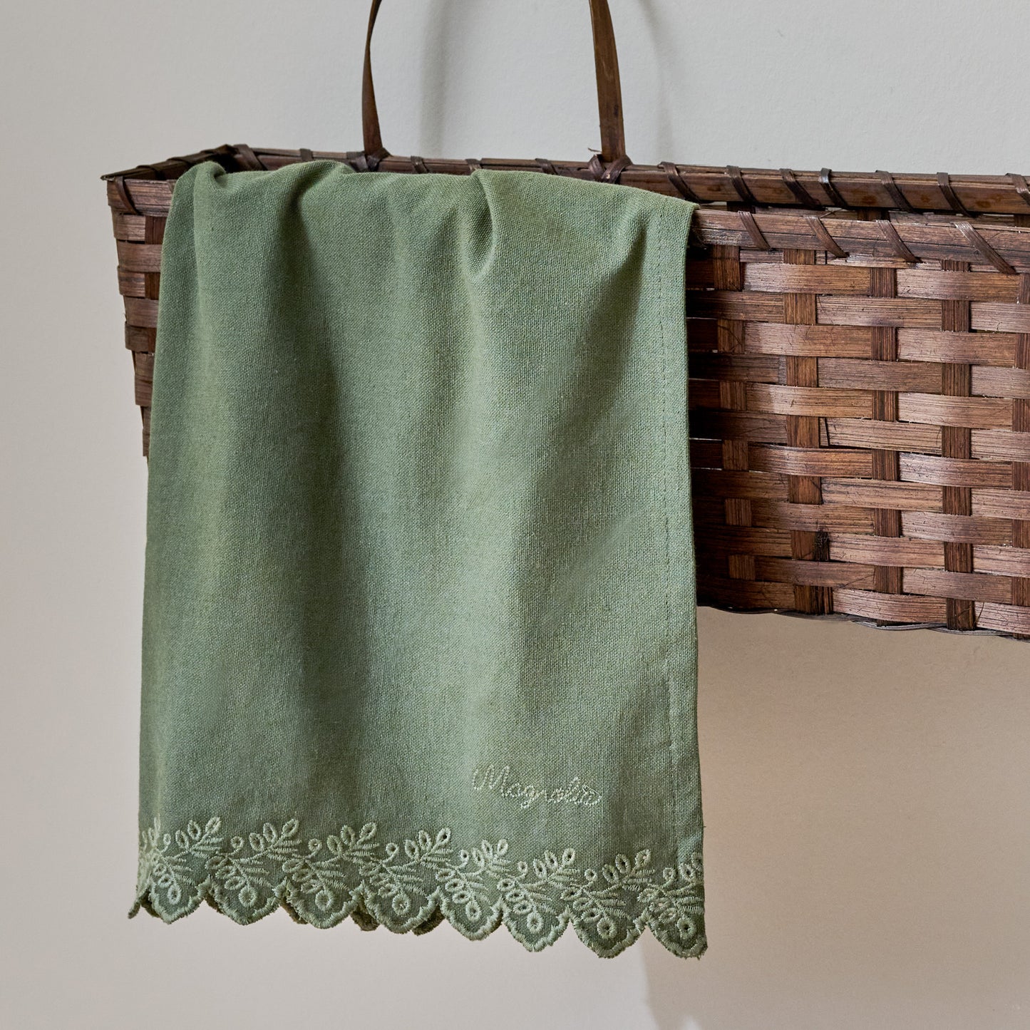 Magnolia Embroidered Scalloped Edge Tea Towel shown in basket on wall
