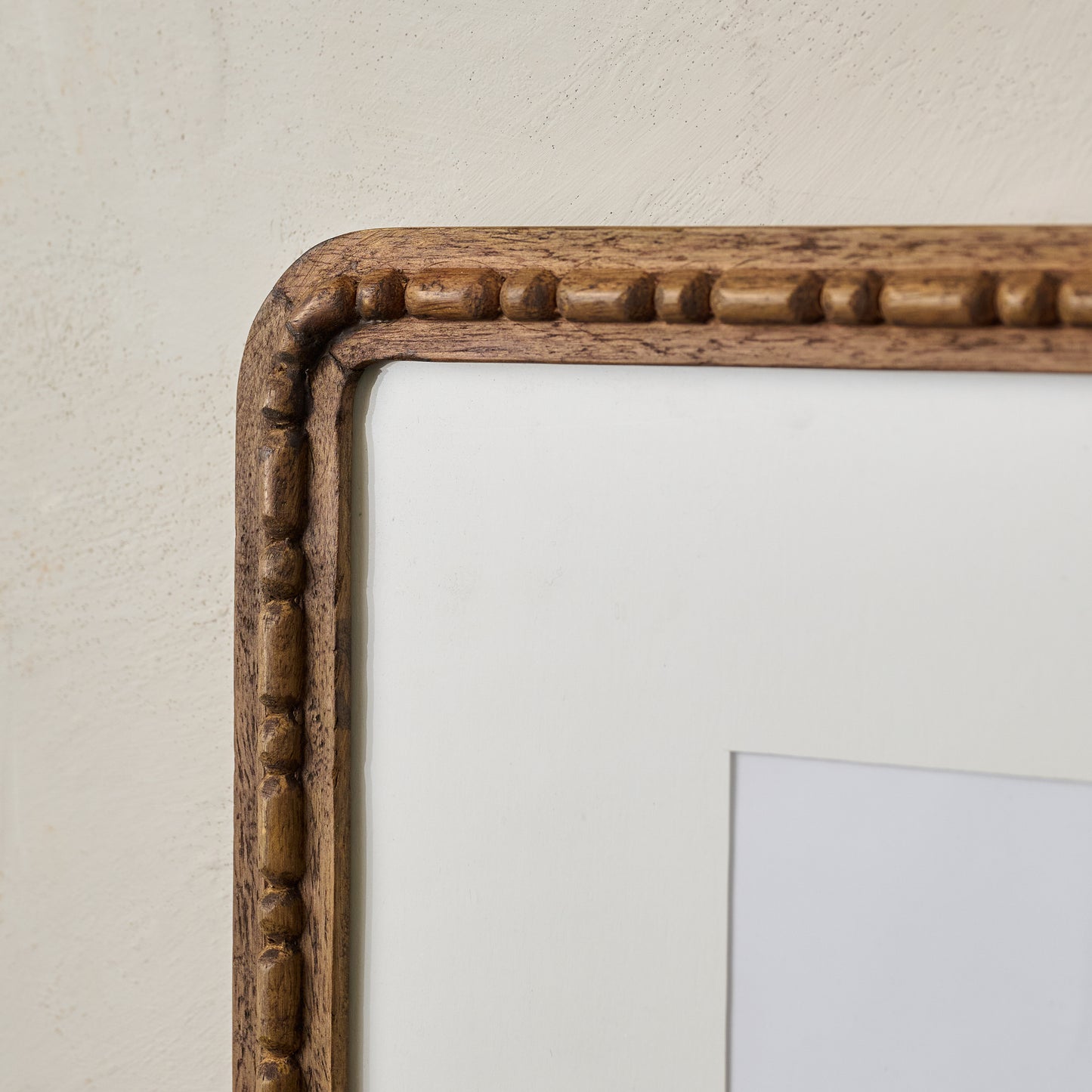 Close-up of a wooden picture frame on a light beige wall.