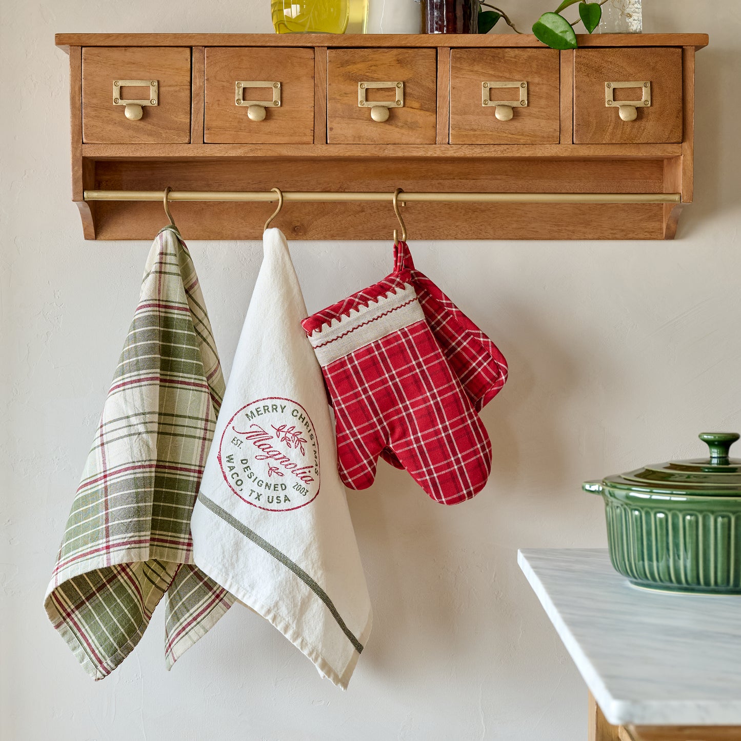 Magnolia Vintage Red Plaid Oven Mitt and Pot Holder Set shown hung on cole wooden wall cabinet with rail