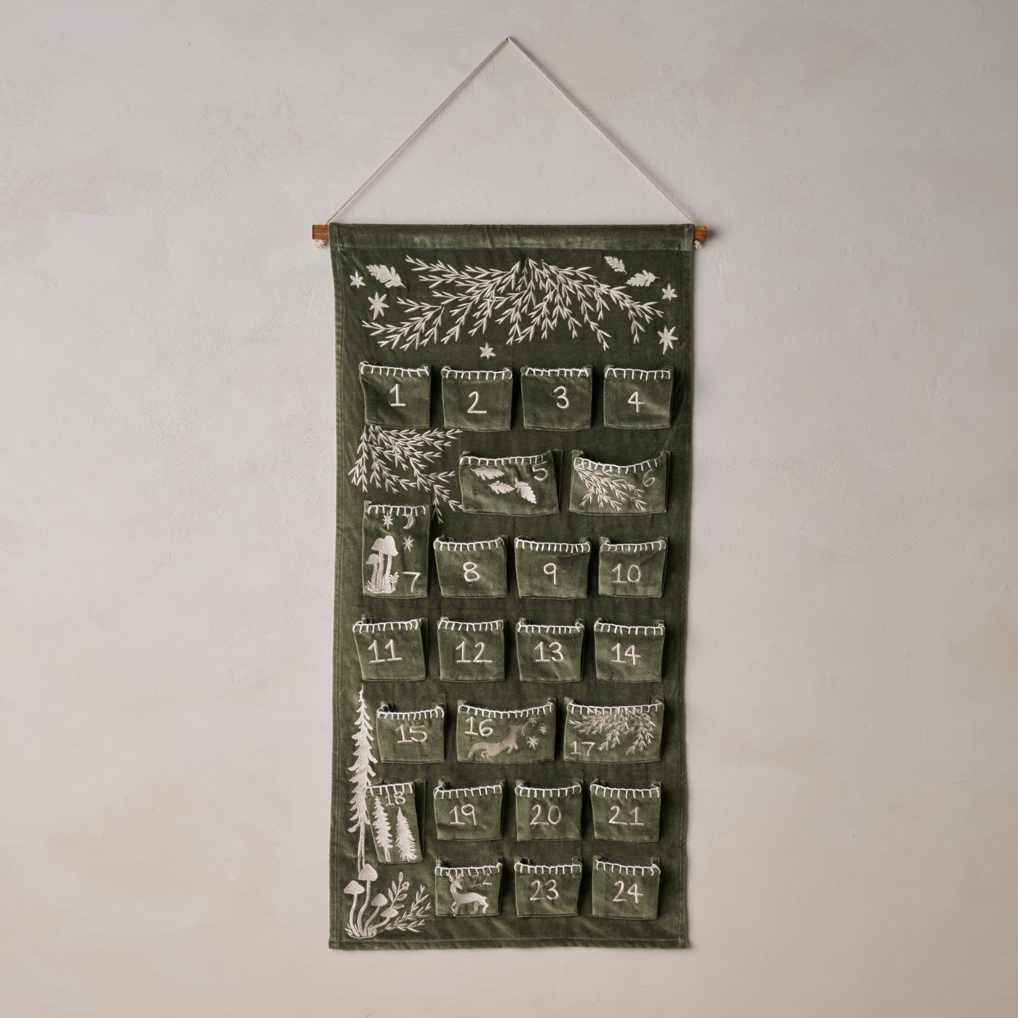 Green advent calendar with nature-themed designs hanging on a white wall.