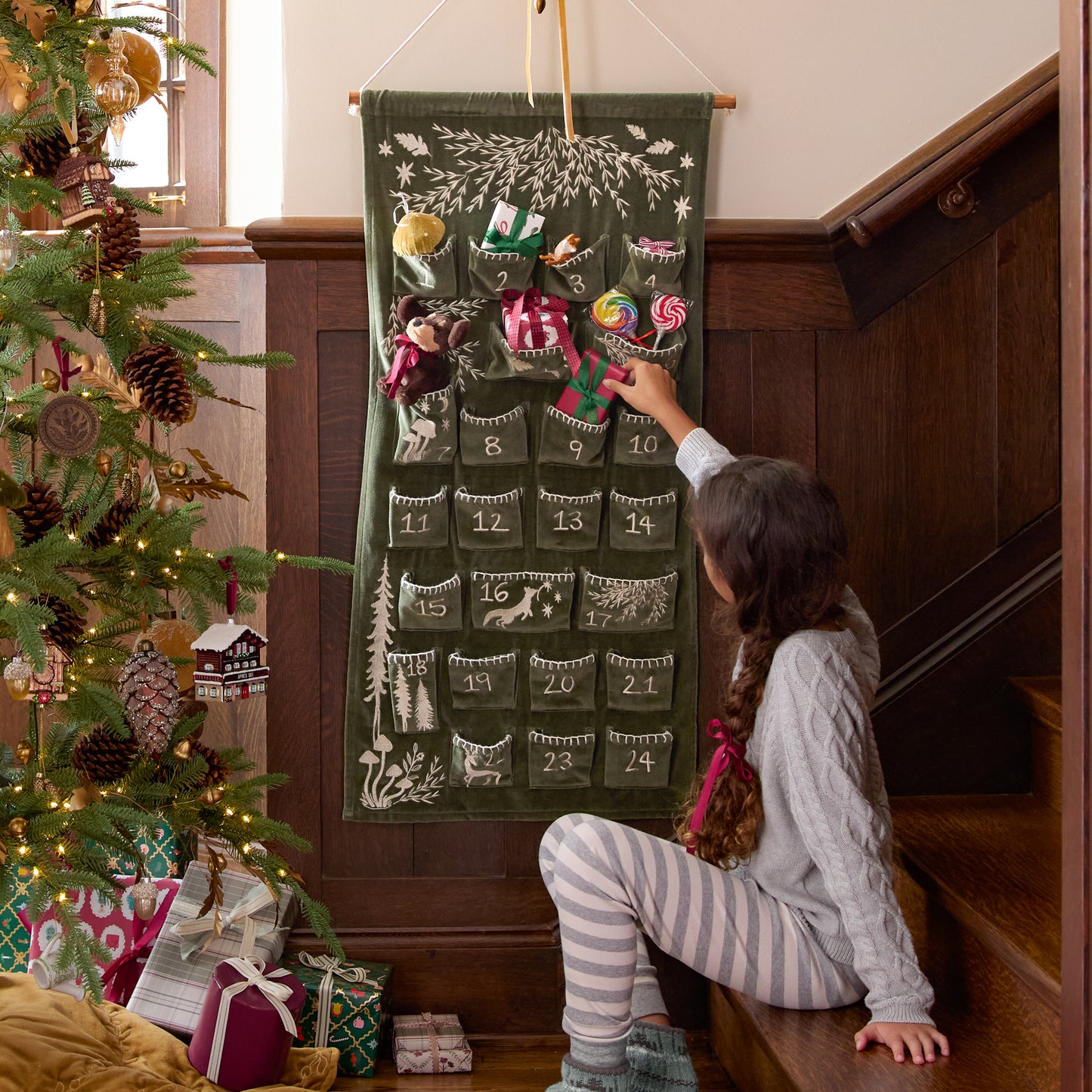 Child interacting with a Christmas advent calendar next to a decorated tree.