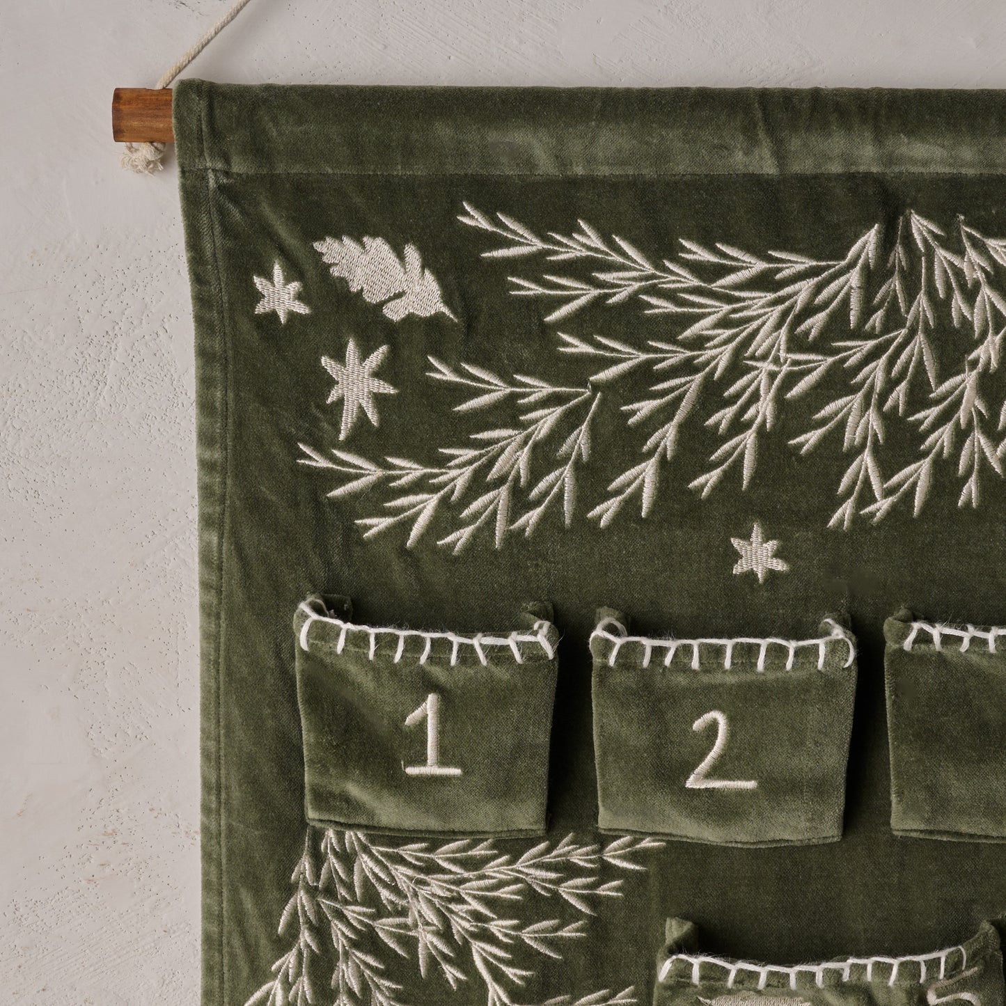 Green fabric wall hanging with embroidered designs and numbers on a white wall.