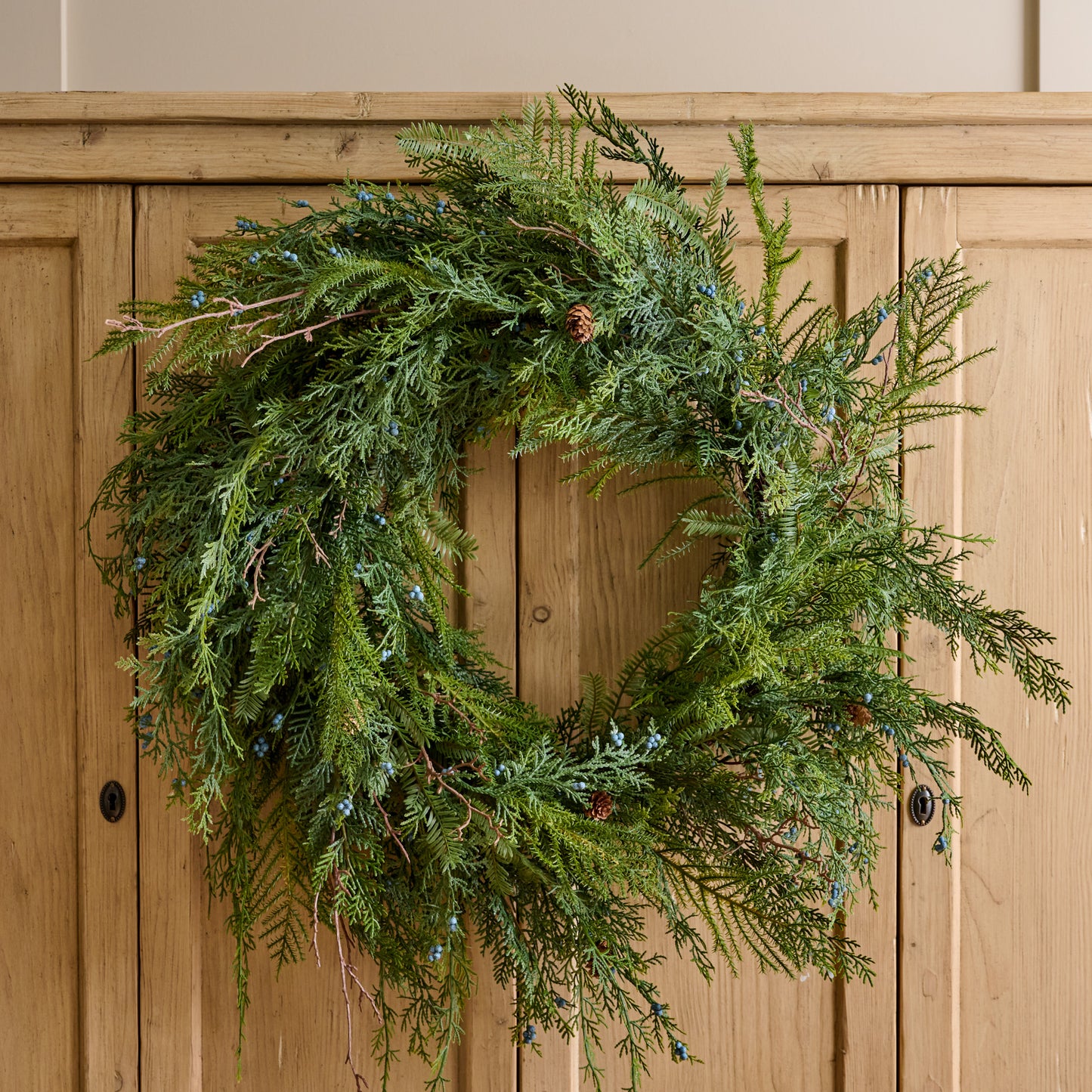 Real Touch Juniper Berry Pine Wreath shown hung on cabinet