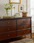 Miller Wooden dresser with decorative items including a vase of flowers and framed pictures in a room.