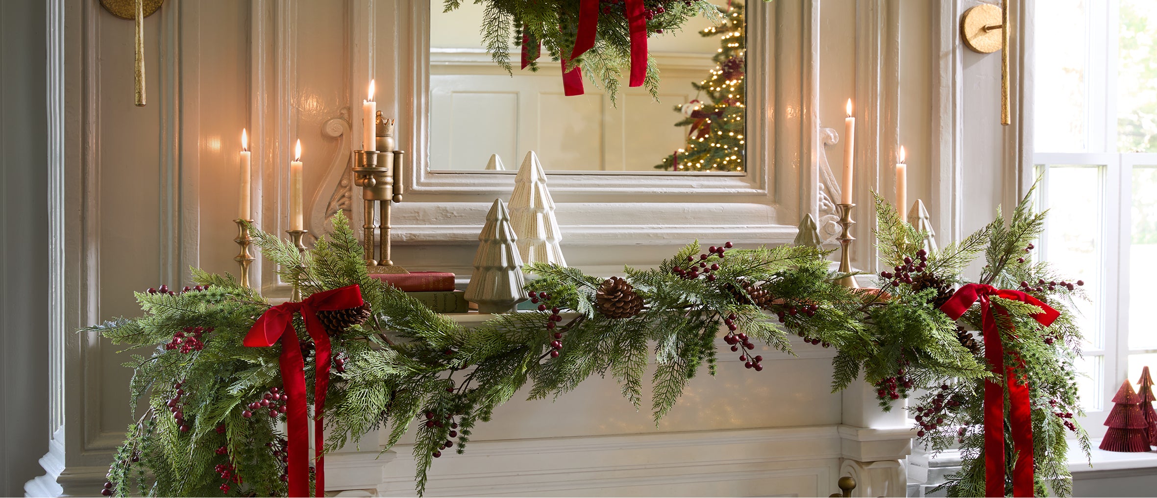 Decorative Christmas mantel with greenery, candles, and red ribbons.