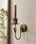 Antique Brass Forged Tulip Wall Sconce with lit taper candle on wall