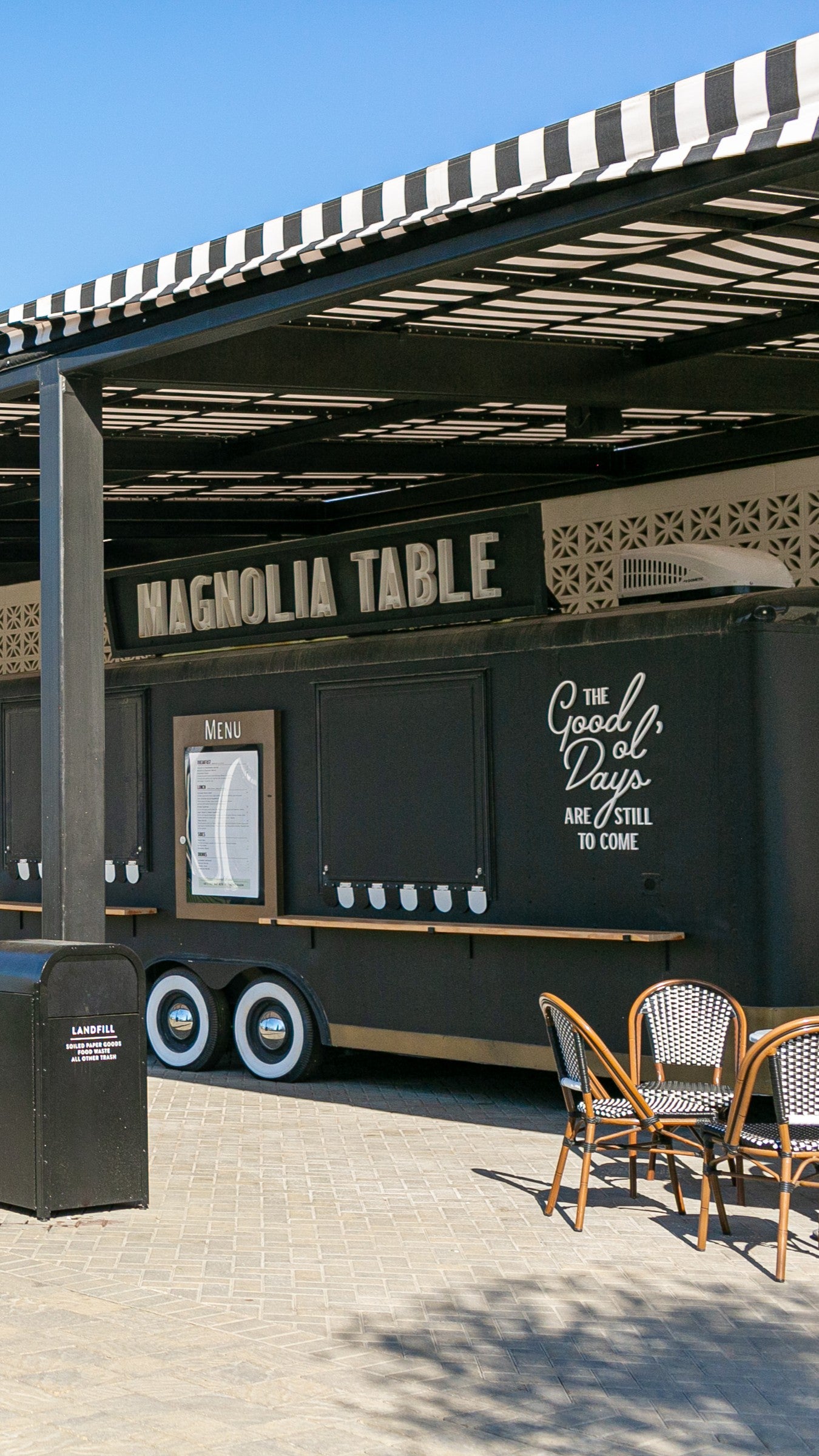 Black food truck with 'Magnolia Table' branding under a striped awning.