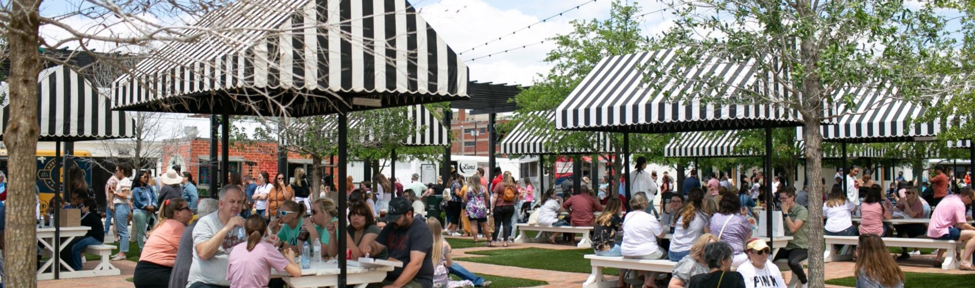Outdoor food truck area at the Silos with people under striped canopies in a park-like setting.