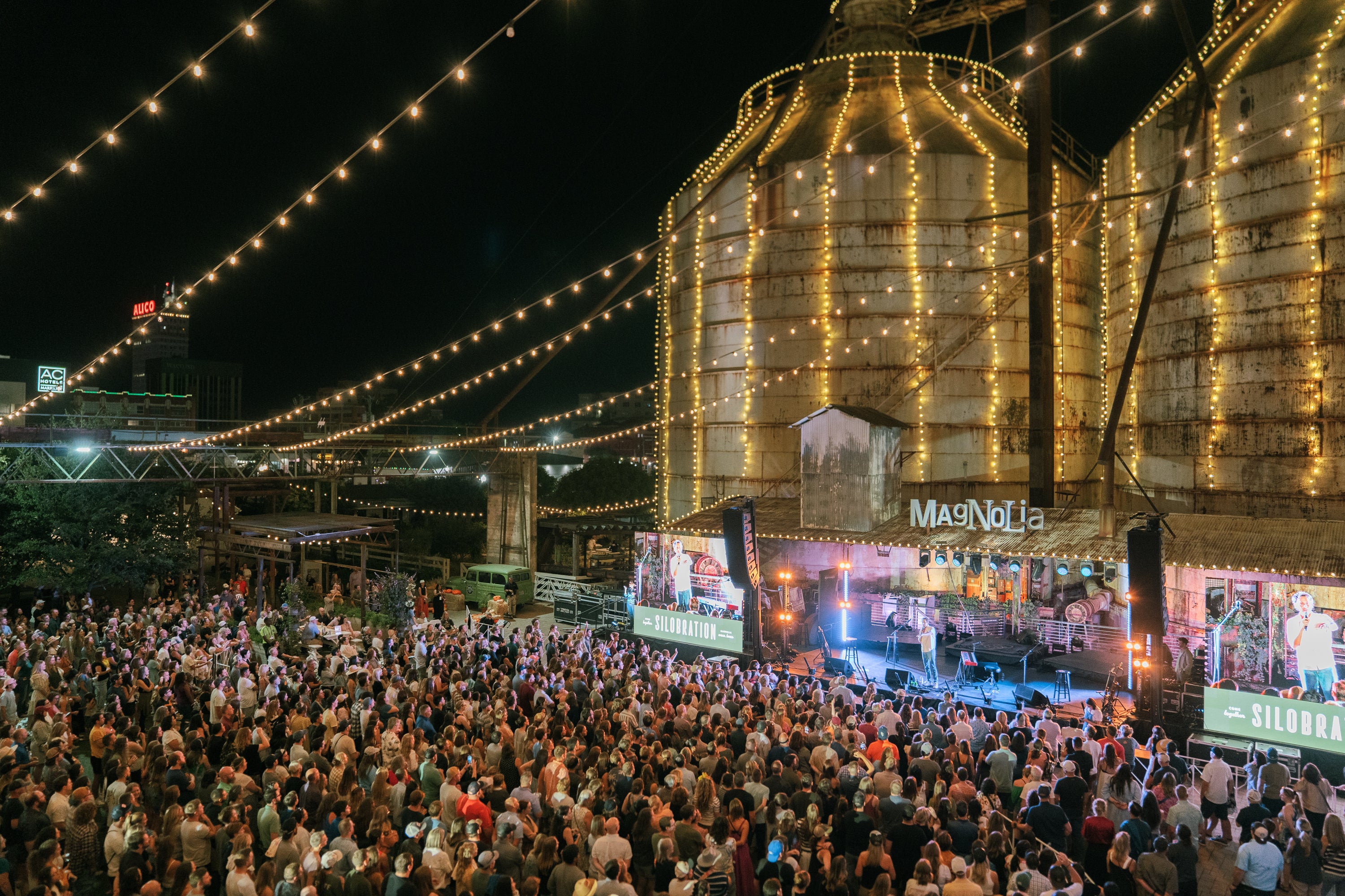 Silobration even in Waco, Texas. Large crowd gathered at a concert event under a large industrial silo structure with lights.