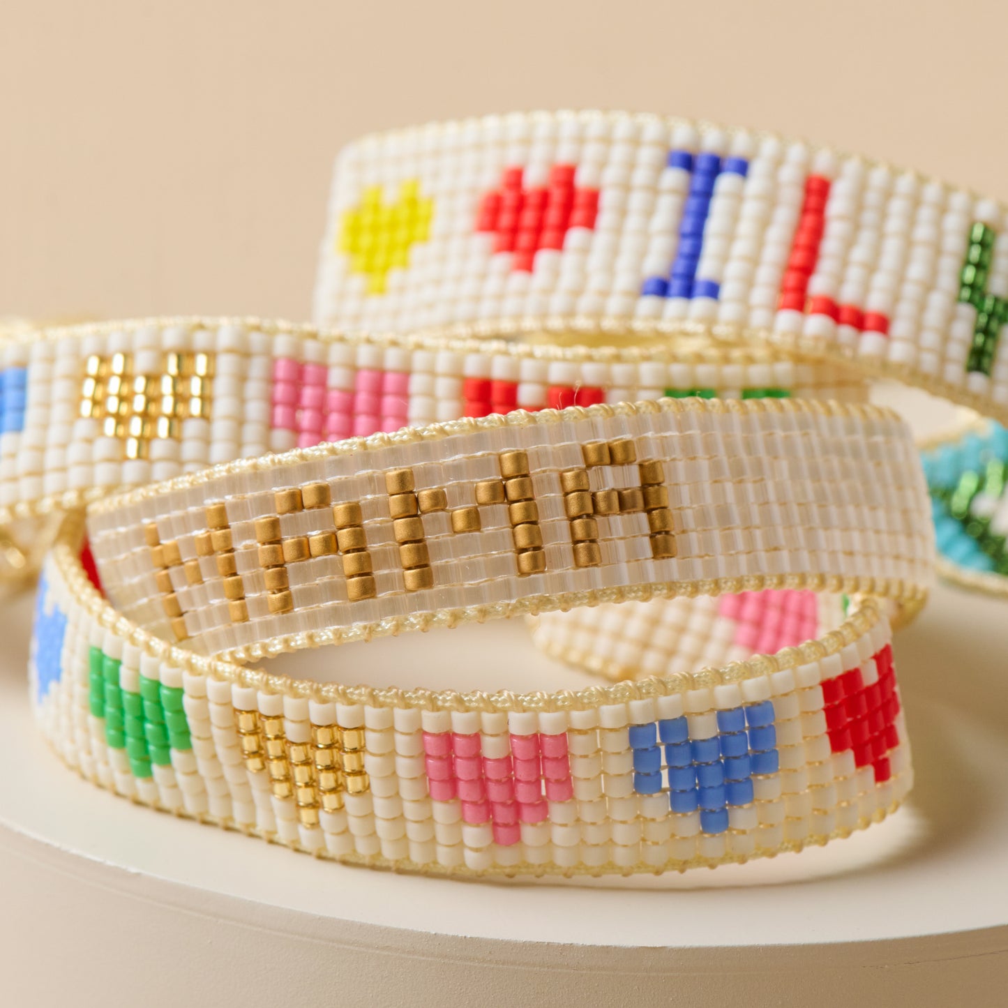 White and gold mama beaded bracelet pictured with rainbow heart beaded bracelets and ILY kids bracelet