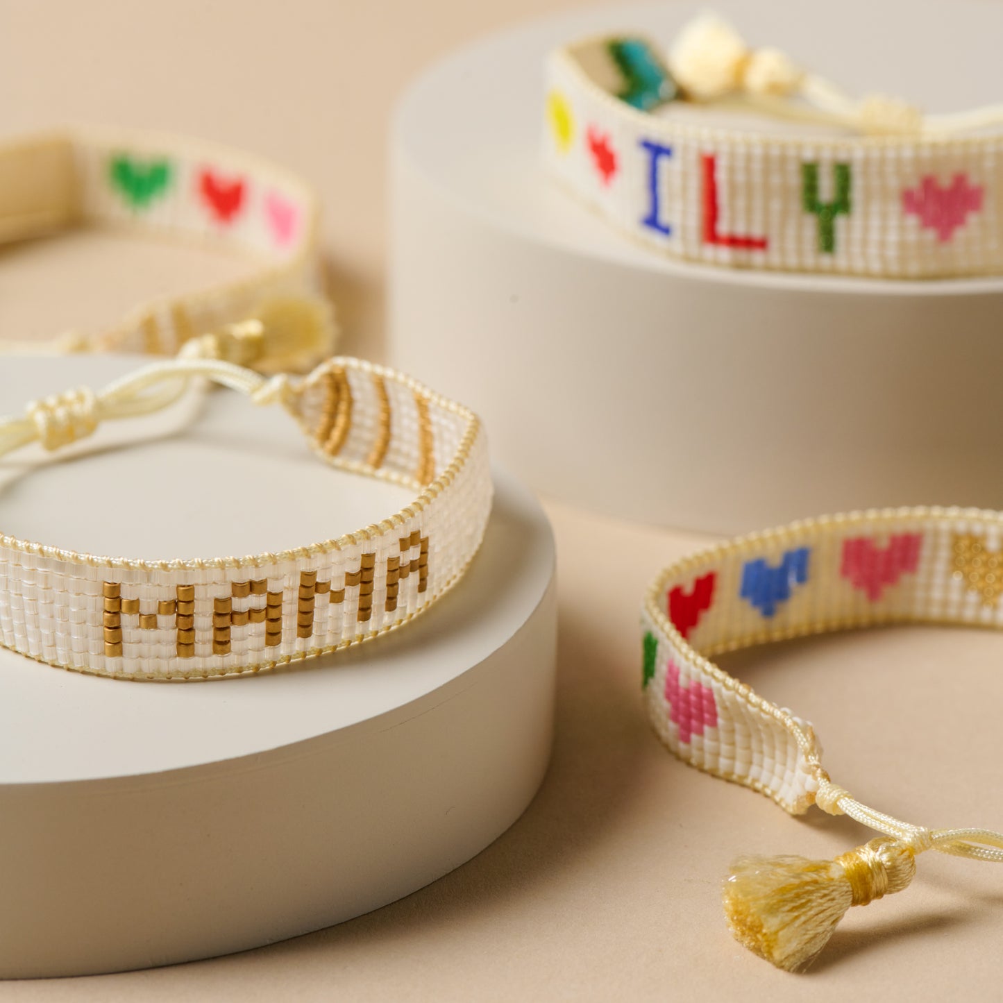 White and gold mama beaded bracelet pictured next to rainbow heart bracelet and ILY kids beaded bracelet