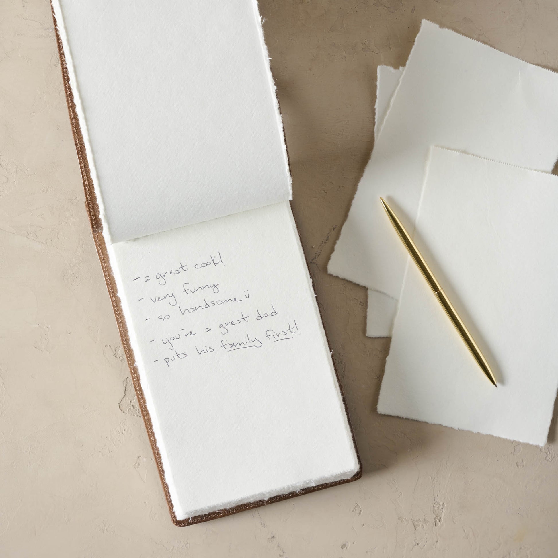Open notebook with blank, unlined pages. Pages have some notes written on them. A gold pen is next to the notebook.