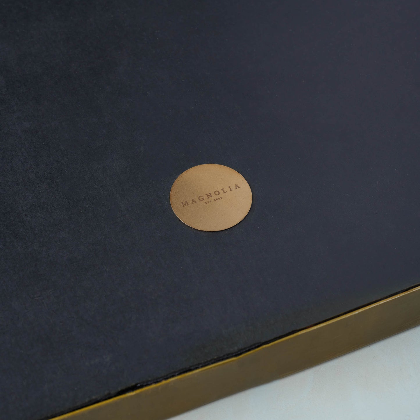 Close up of gold Magnolia circle logo on back of Dorian Brass Mantle Mirror