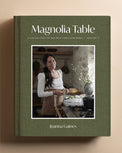 The book 'Magnolia Table: A Collection of Recipes for Gathering Volume 3' by Joanna Gaines, featuring an olive green textured cover with a central color photograph of a woman in a rustic kitchen, displayed on a warm beige background.