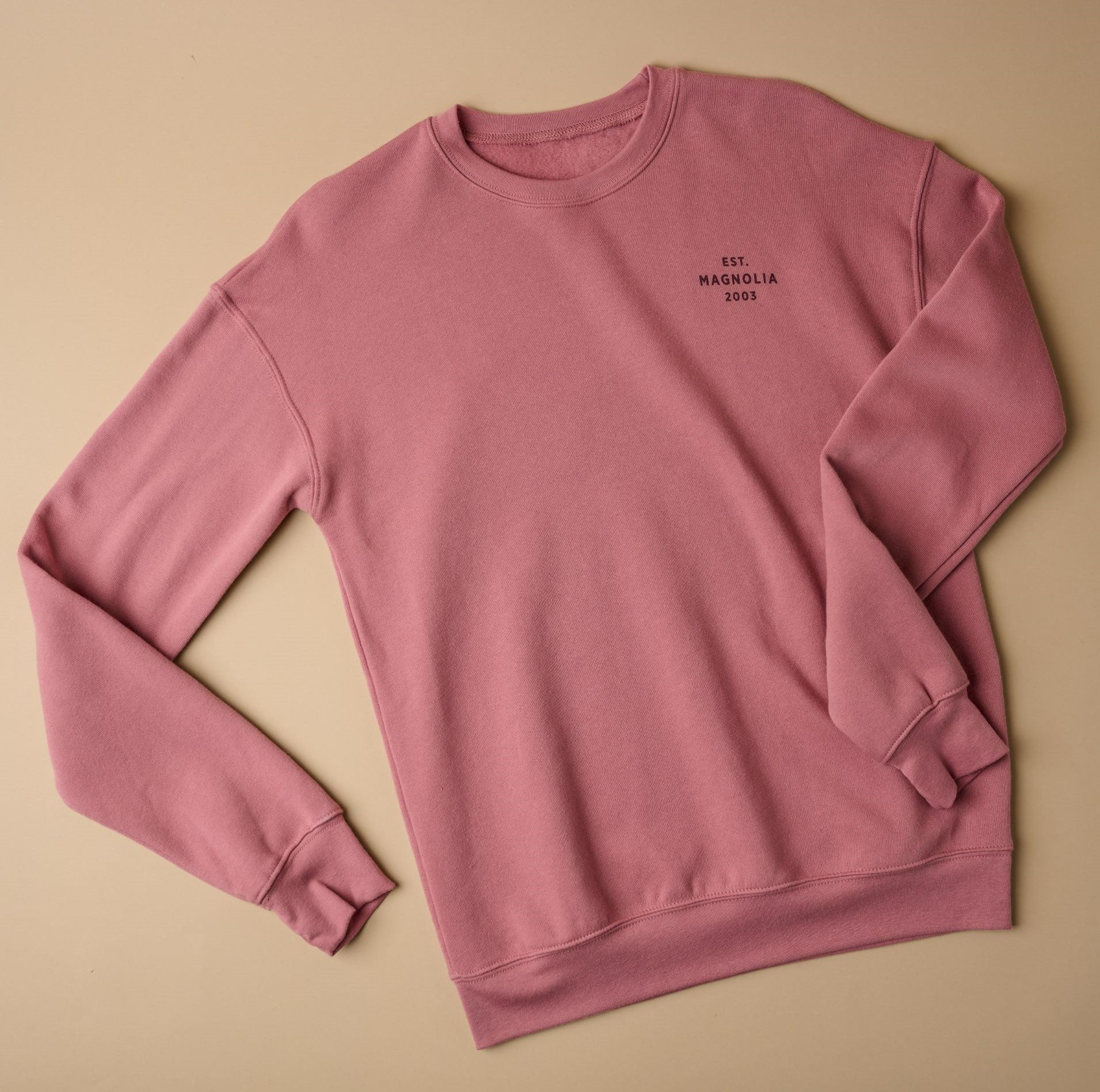 Top view of mauve sweatshirt that reads EST Magnolia 2003 on left chest in plain font, all capital letters. Text color is maroon.