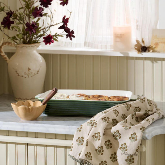 A fresh batch of cinnamon rolls are being made in this kitchen using pieces from our Cottage Collection, like the Forest Green Baking Dish and Oatmeal Block Printed Tea Towel.