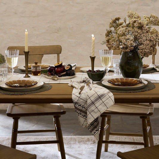 Fall tablescape with yellow stems in a glazed black vase centered on the table.  Four place settings that include placemat, dinner plate and salad plate in fall colors.