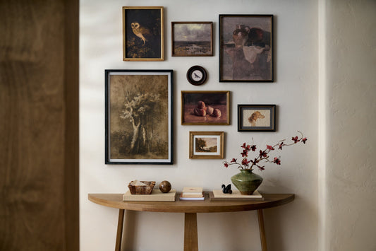 Gallery wall of framed art and wall decor above a console table with a green vase and maroon blossoms sticking out.