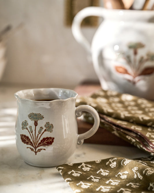 A coffee mug with a floral motif sits on a counter next to a block-printed tea towel from Magnolia.