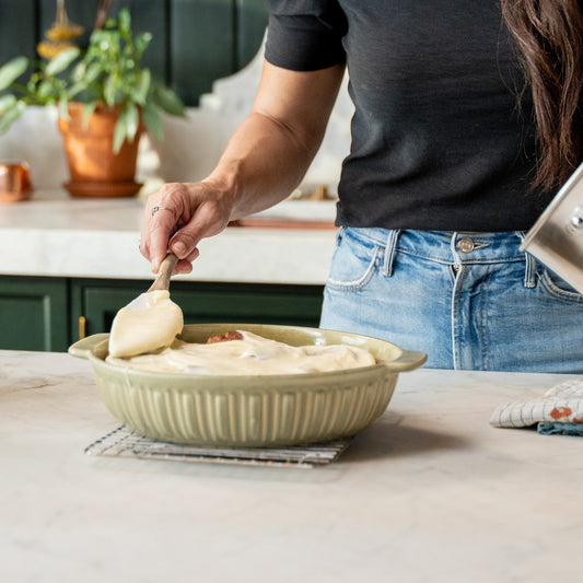 Joanna Gaines in her butler's pantry with a baking pan full of fresh cinnamon rolls.  She is standing at her kitchen island spreading the homemade cream cheese icing on the pan of fresh cinnamon rolls.