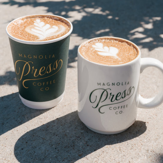 Magnolia Press Coffee in a green to go cup and a white ceramic mug.