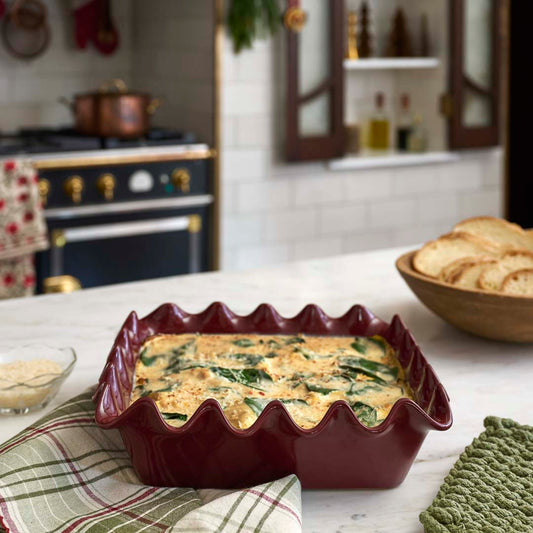 Maroon scalloped baking dish on a marble countertop with crostinis and winter tea towels.