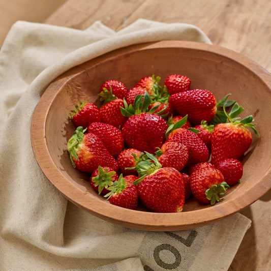 fresh strawberries in a wooden bowl, on top of a Magnolia tea towel