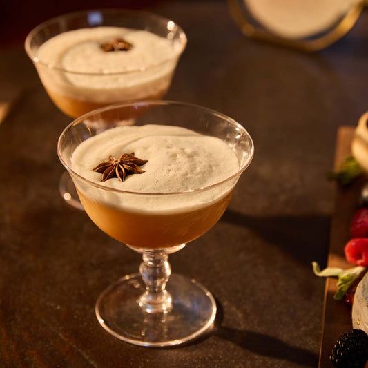 Two etched glass coupes filled with an apple cider- and maple-infused whiskey sour and garnished with star anise pods.